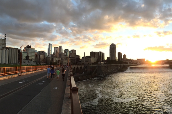 Minneapolis skyline at the St. Anthony bridge at sunset. A family is walking away from the camera, crossing the bridge.