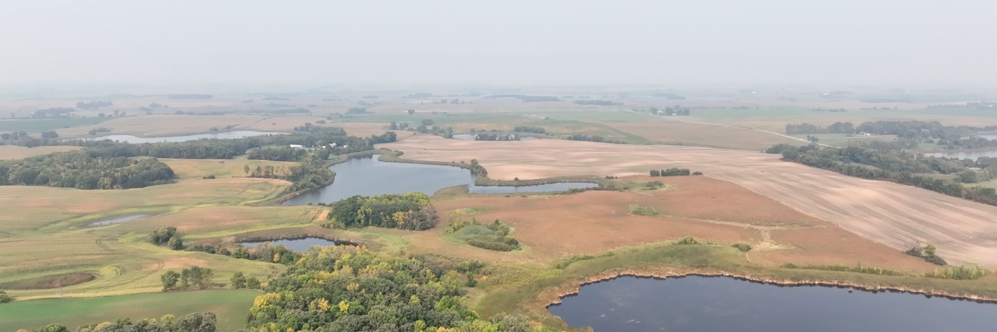A hazy sky over a landscape of fields and woods.