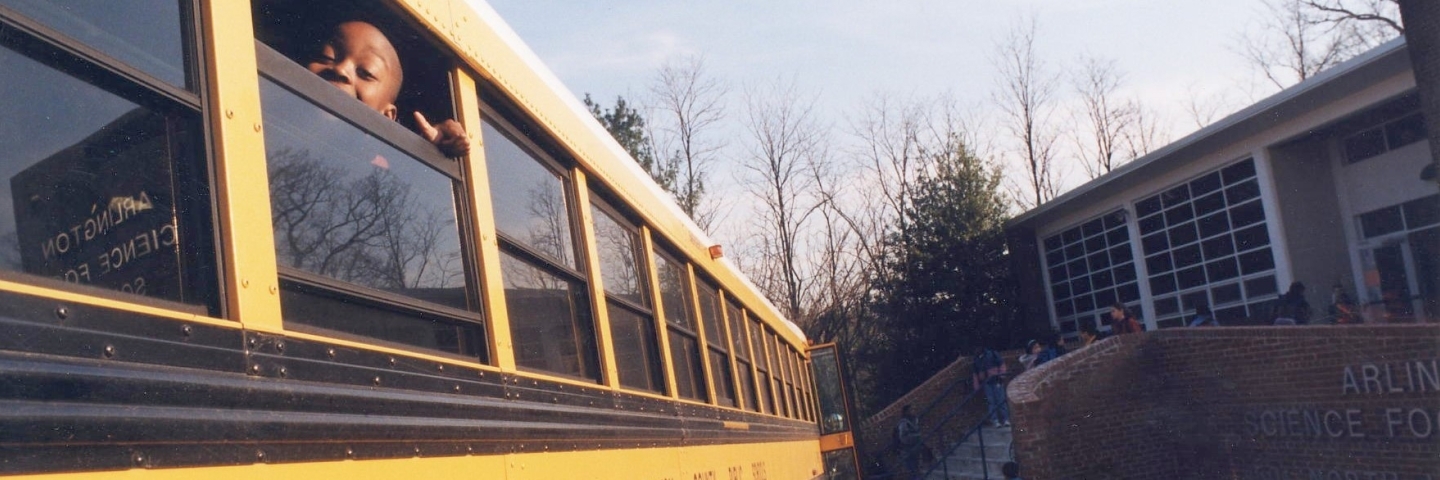 School bus pulling up to school. A window is down and a child is looking out.