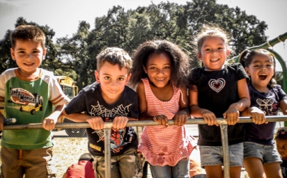 Five young children on a playground smiling and laughing as they look at the camera.
